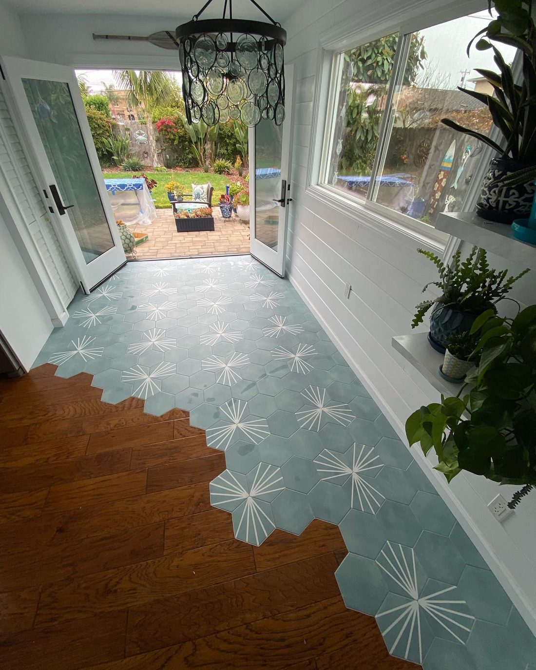 Pale teal hexagon tiles with a white starburst pattern running into a wood floor in a staggered edge, in a bright sunroom opening onto a garden.