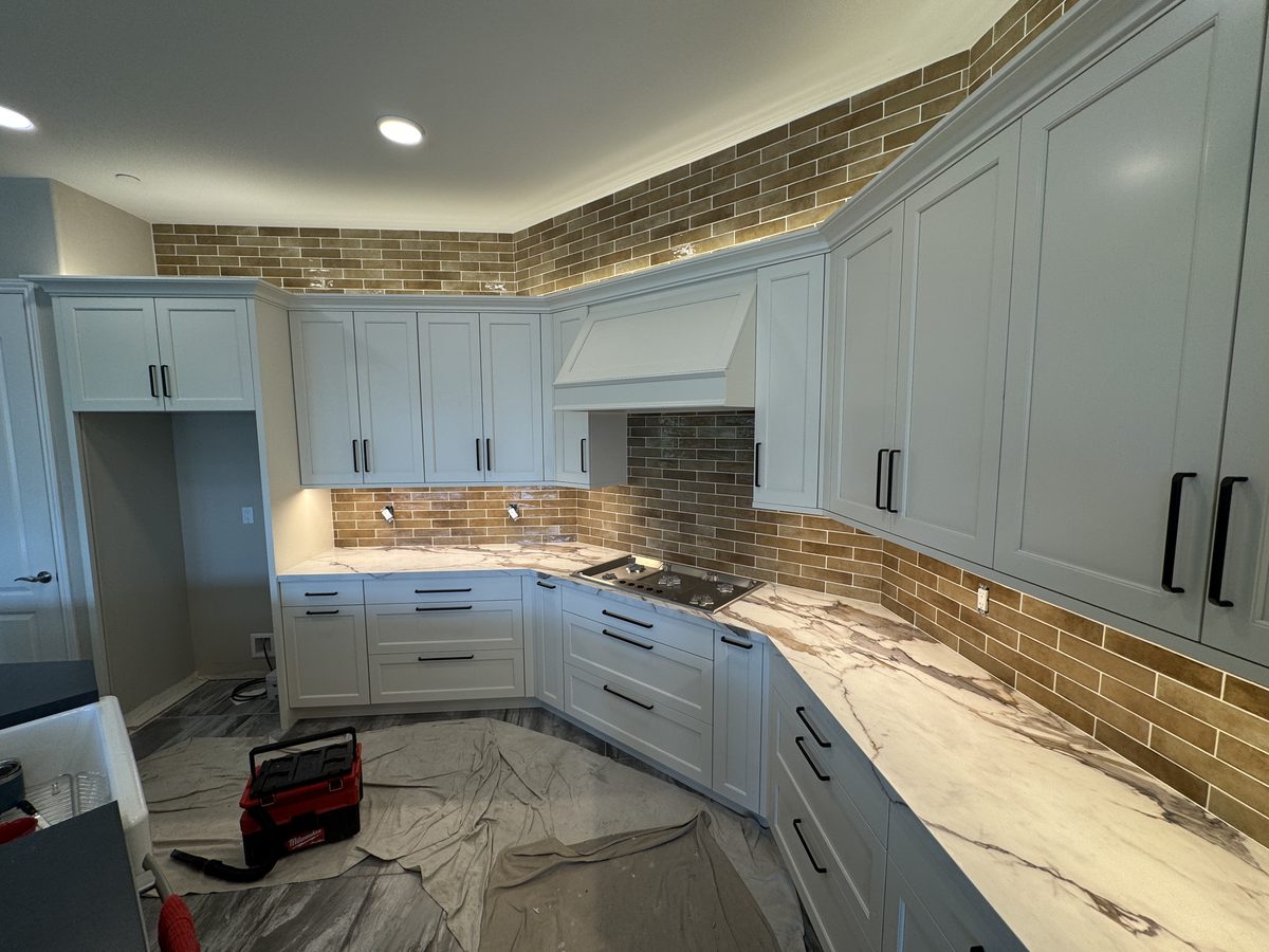 A long kitchen with gray-blue cabinets and a brick-look tile backsplash running under the upper cabinets.