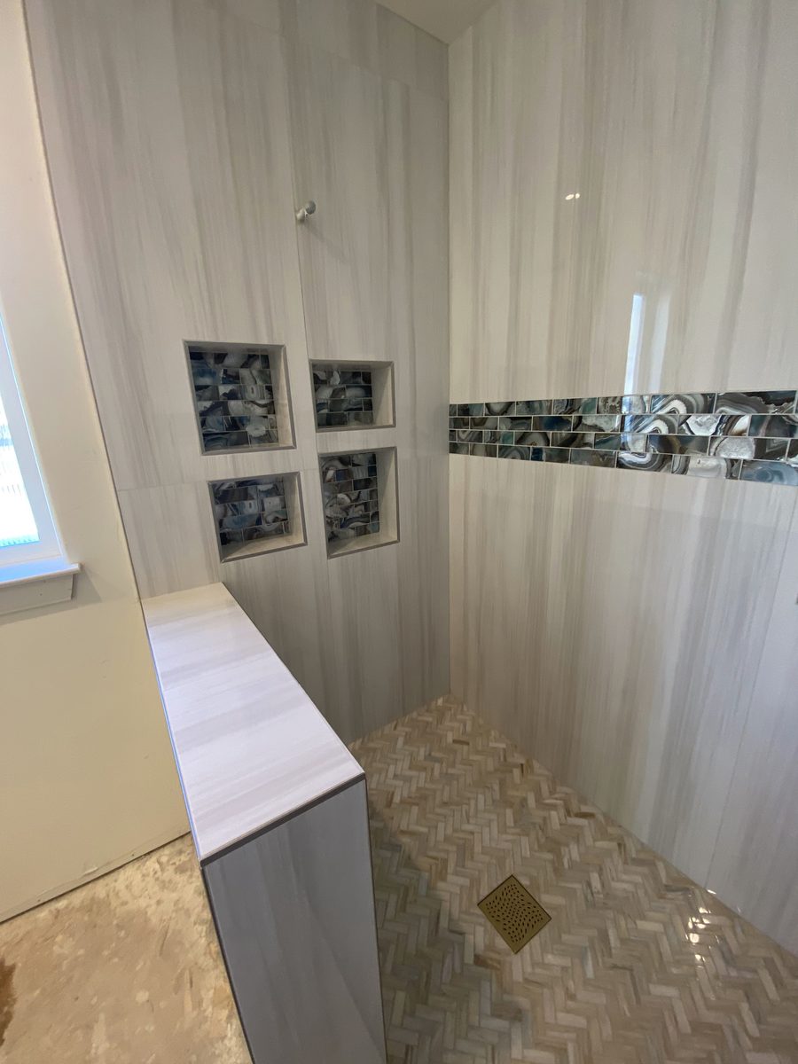 A shower with three glass-mosaic niches, a matching accent band and a herringbone floor.