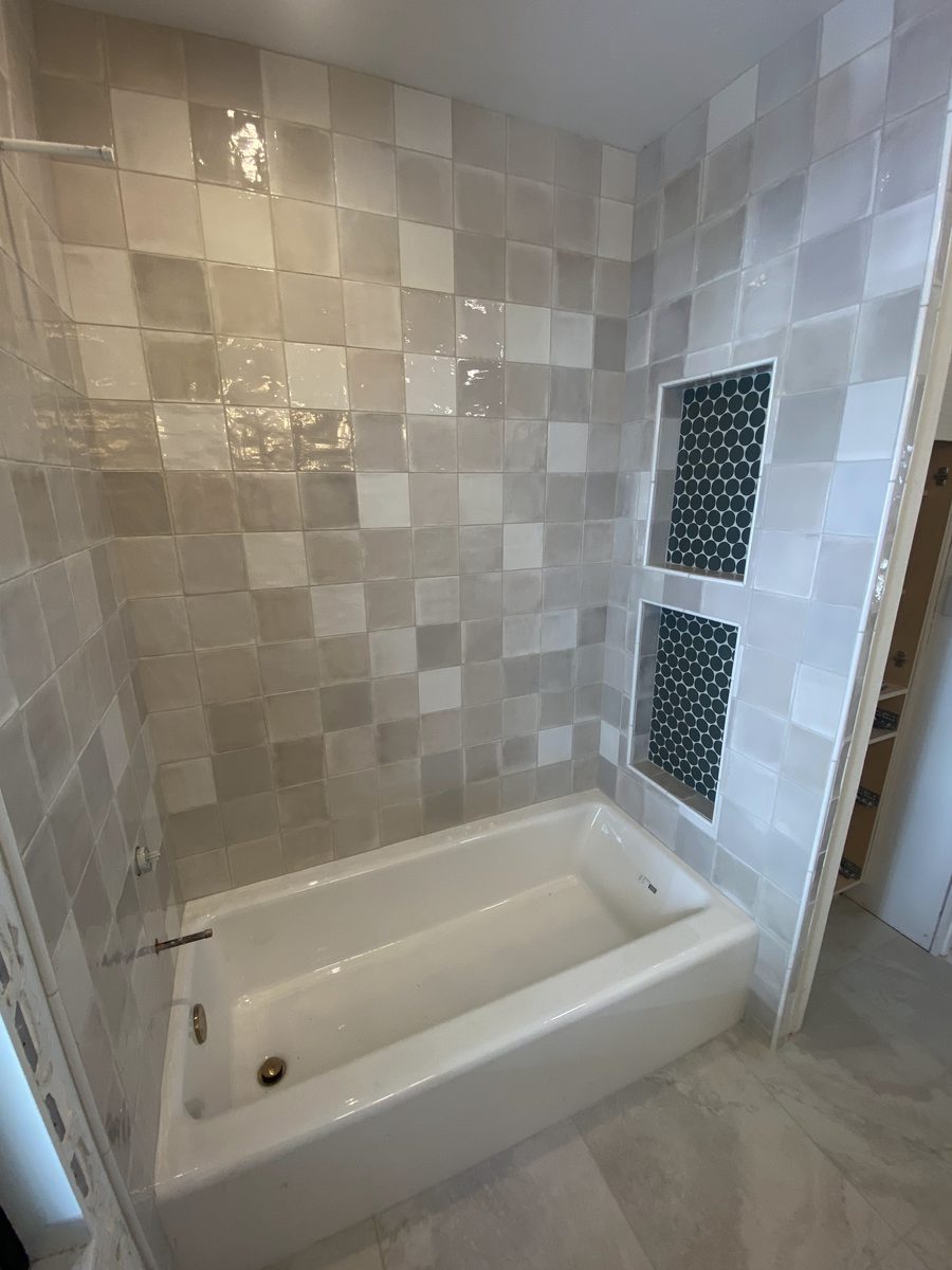 A tub surround in glossy square tile with two dark green hexagon-mosaic niches.